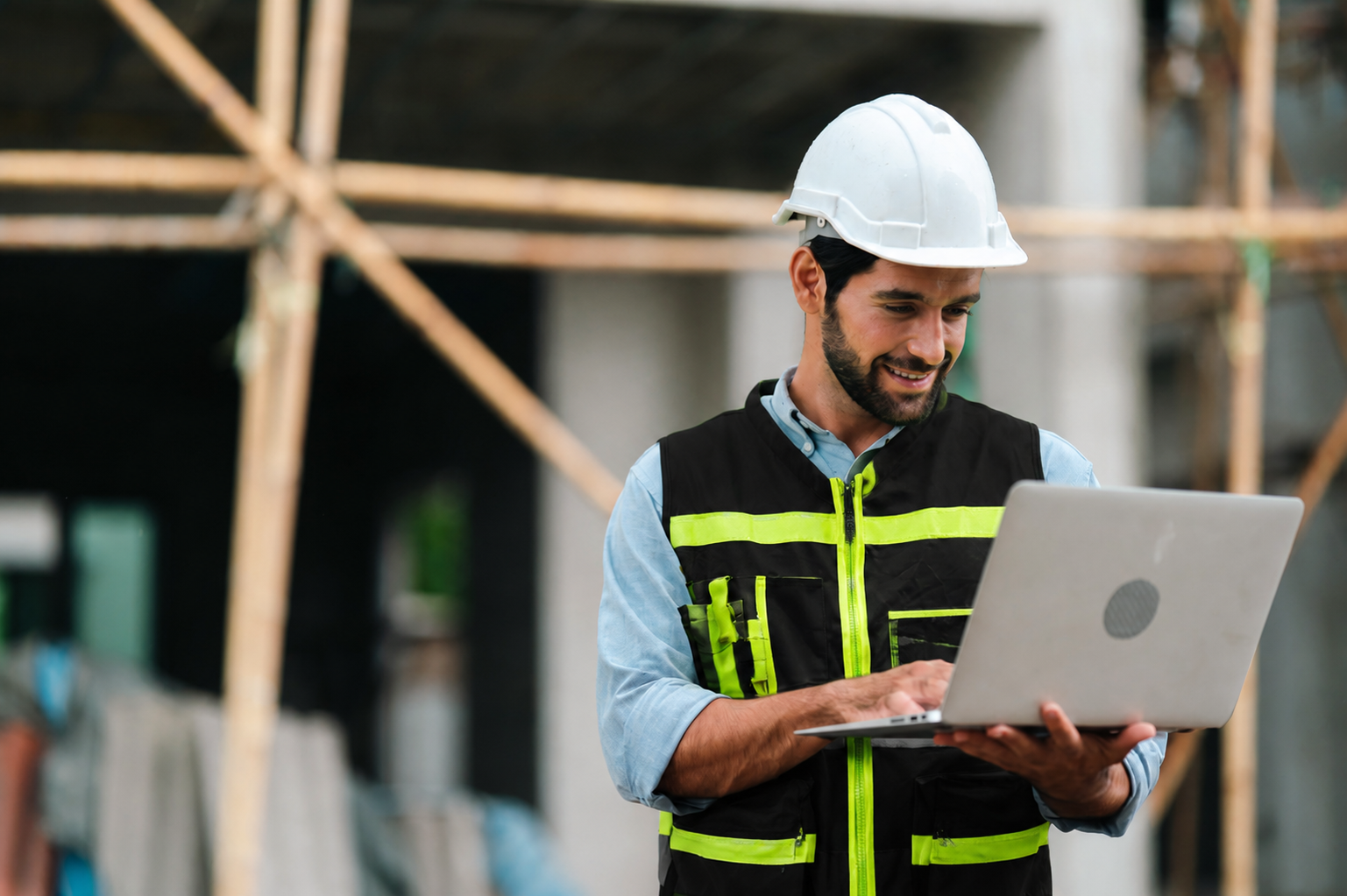 Builder in a hard hat and high-visibility vest working on a laptop at a construction site